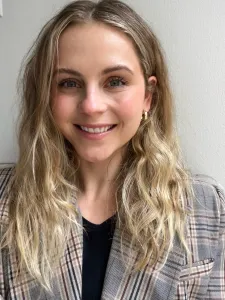 Woman with long blonde hair wearing a plaid blazer and black top, smiling while facing the camera.