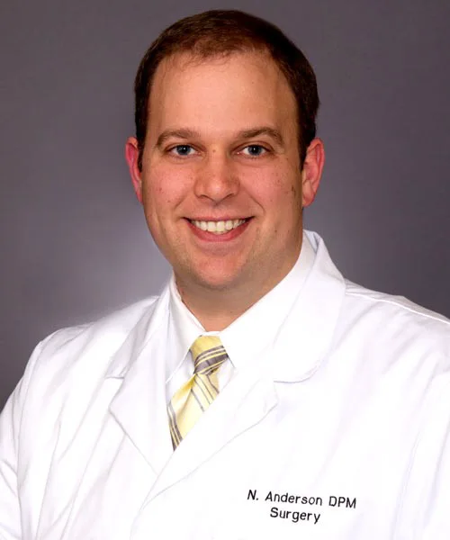 Orthopedist Dr. Nicholas Anderson smiling in his white coat and gold striped tie