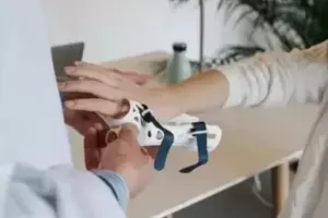 A person helps another individual adjust a white and blue wrist brace on their hand in a clinic.