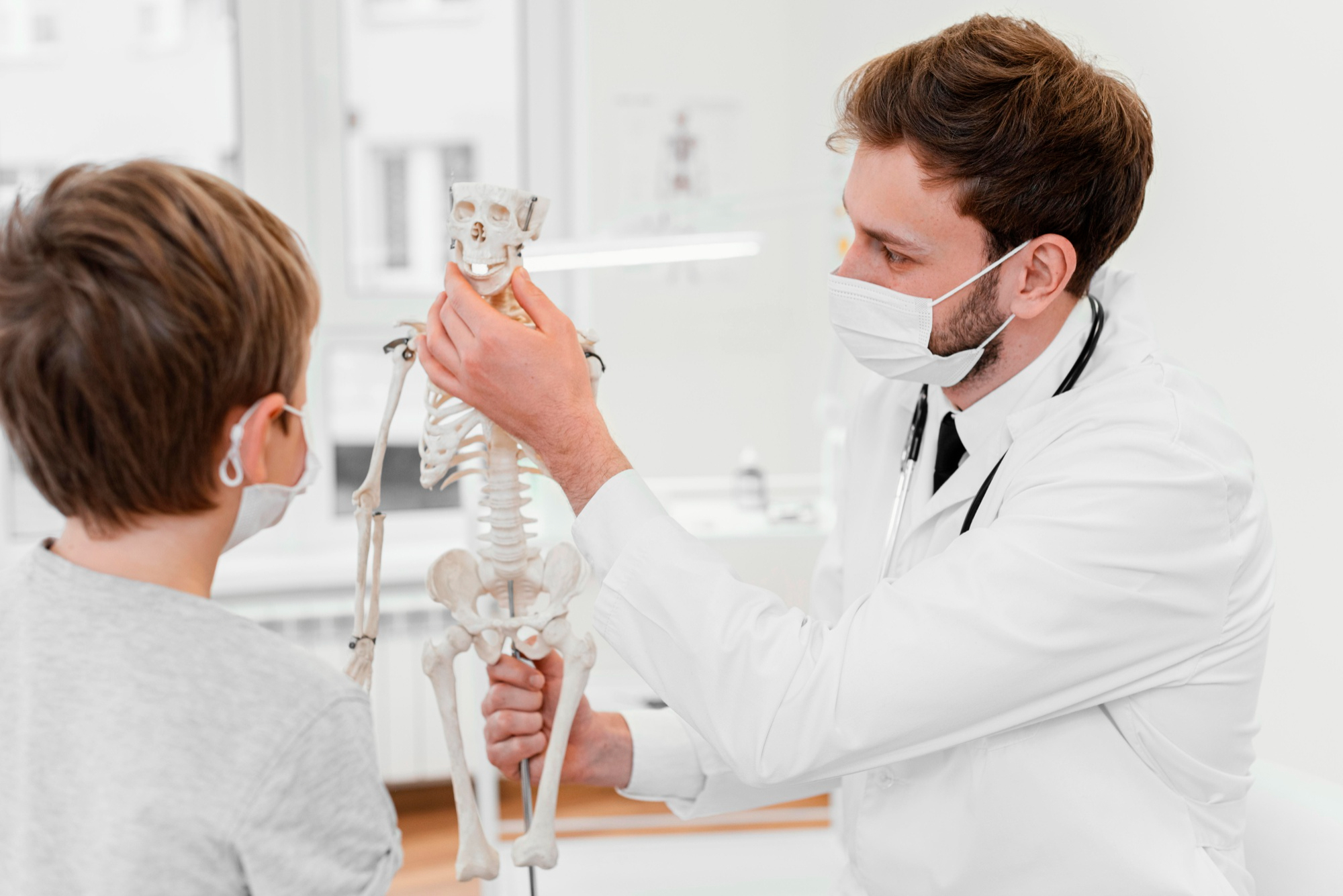 Orthopedist in his white coat using a model skeleton to explain care to a pediatric patient