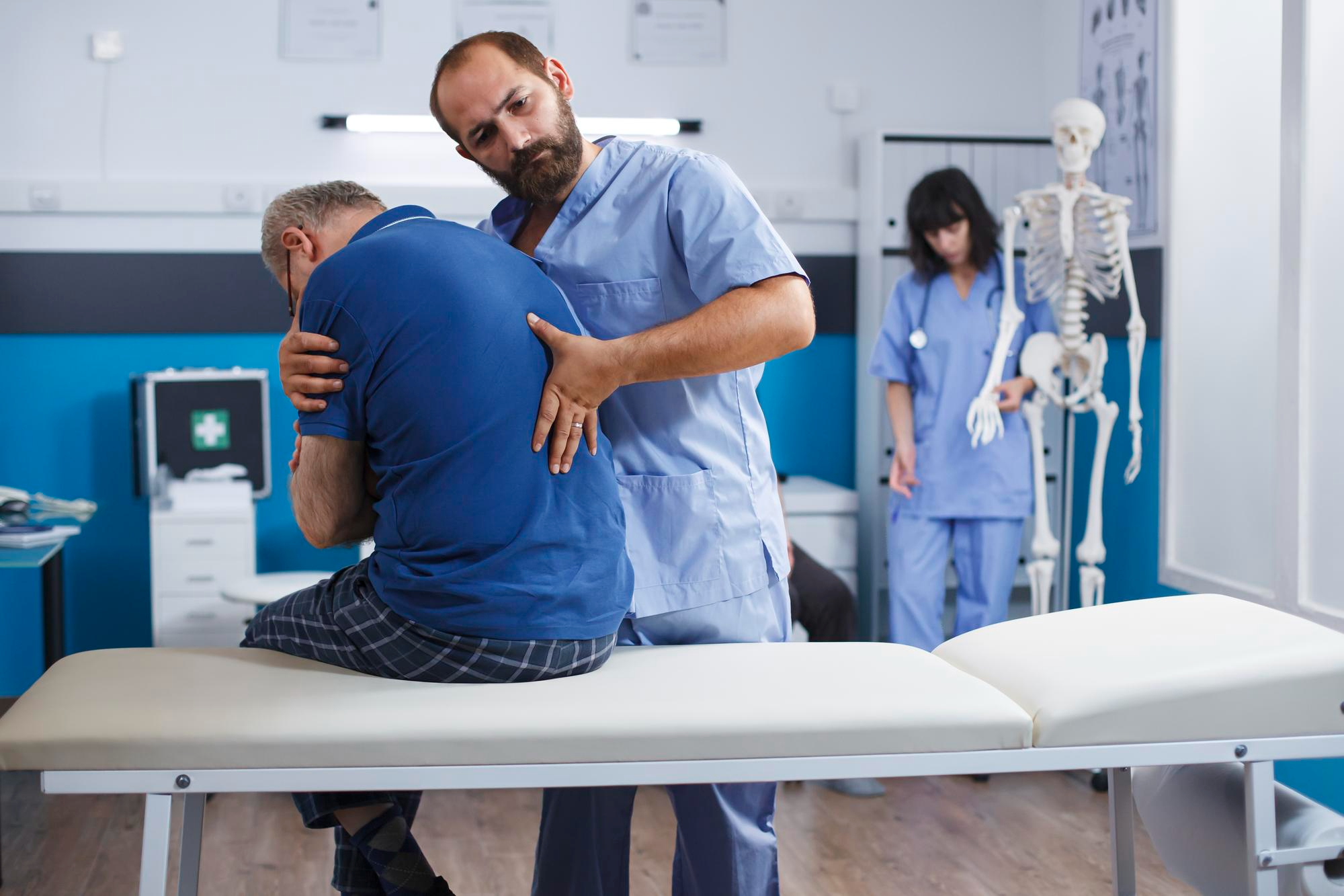 Orthopedic doctor in blue scrubs performing a spinal patient on a middle aged man