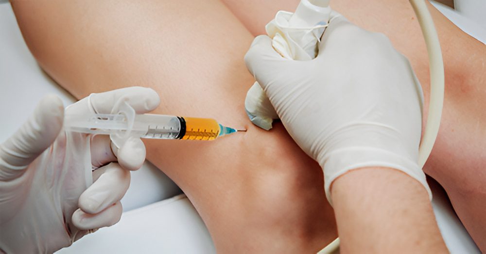 A medical professional injects medicine into a patient's knee using a syringe, with an ultrasound.